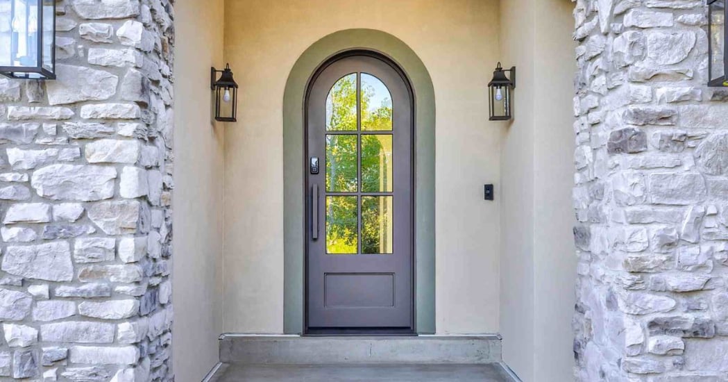 Home entryway with arched front door, stone walls, and exterior lighting in Olympus Cove, UT by Marshall Homes