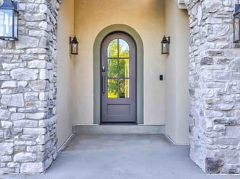 Image of home entryway with arched front door, stone walls, and exterior lighting in Olympus Cove, UT by Marshall Homes